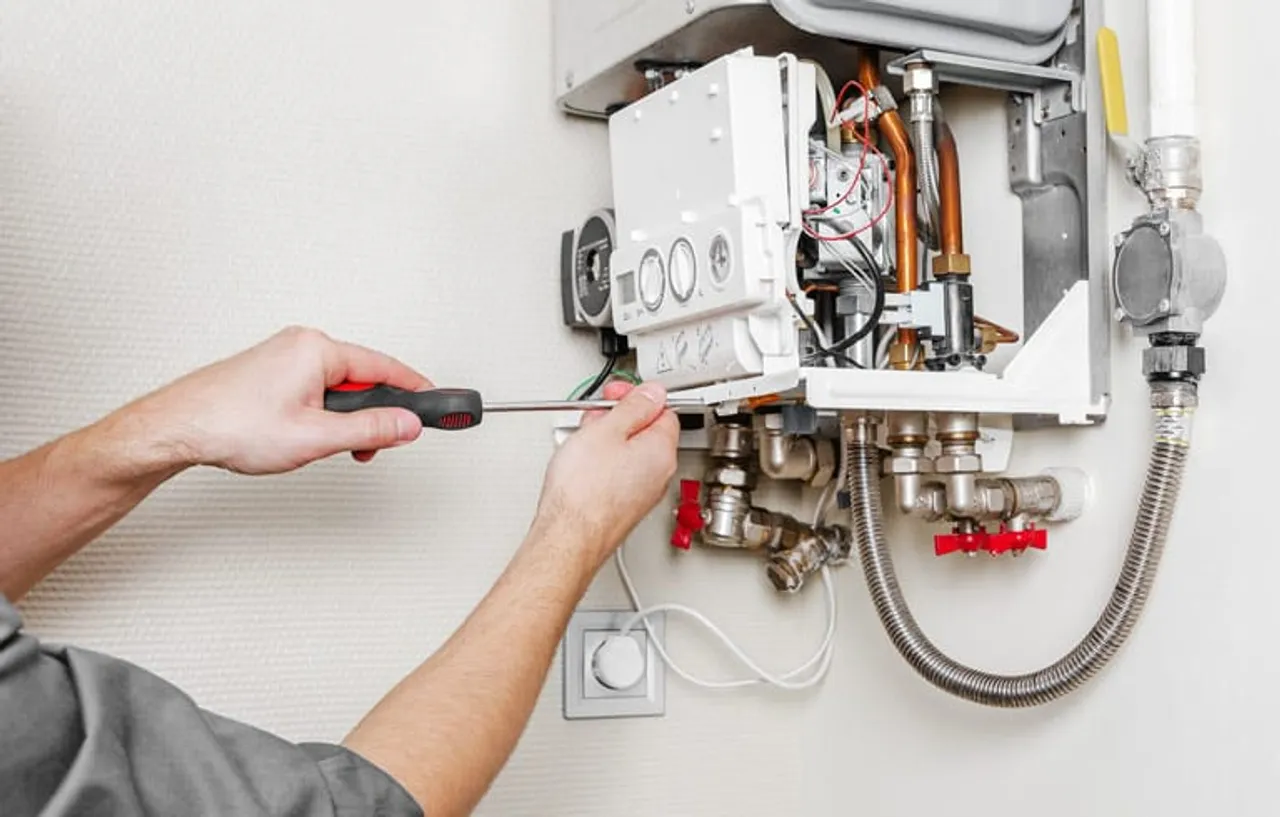 Hands using a screwdriver on copper and flexible water connections at a wall-mounted unit