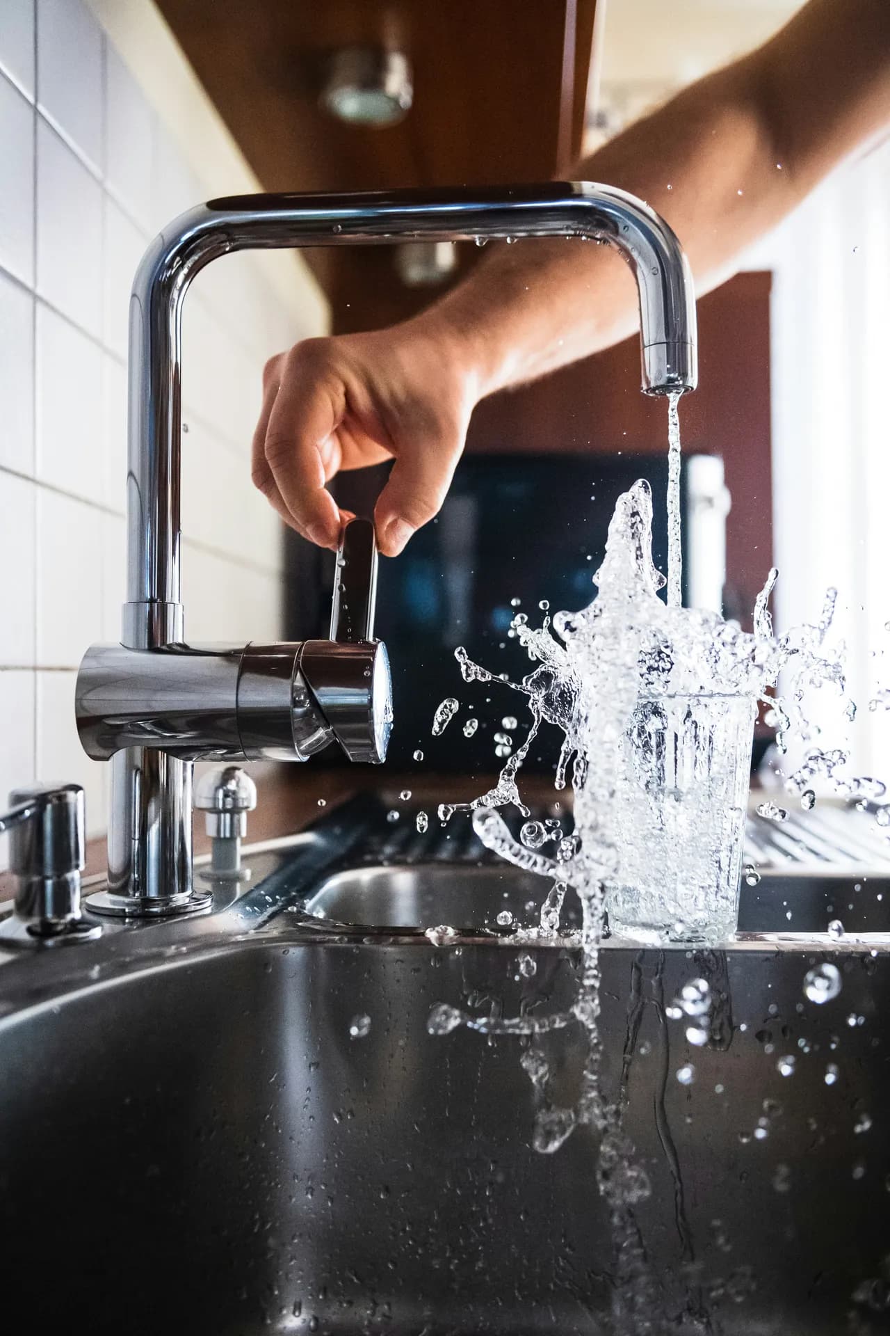 Homeowner filling a glass of water at a kitchen faucet